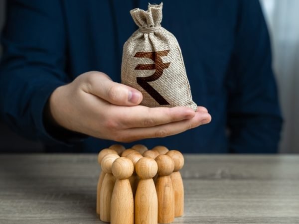 A man is holding a indian rupee money bag over a group of people figurines. Political lobbying. Organization of the community budget. Payment for labor. Generation of funds from cooperation.